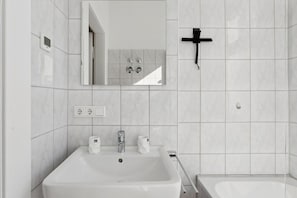 Un bany amb un lavabo blanc, un mirall i una creu negra a la paret.