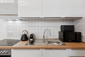 A modern kitchen with white cabinets, a stainless steel sink, a kettle, a toaster, and a microwave. - Arbio I Modern Art Suite for 6 (Leipzig)