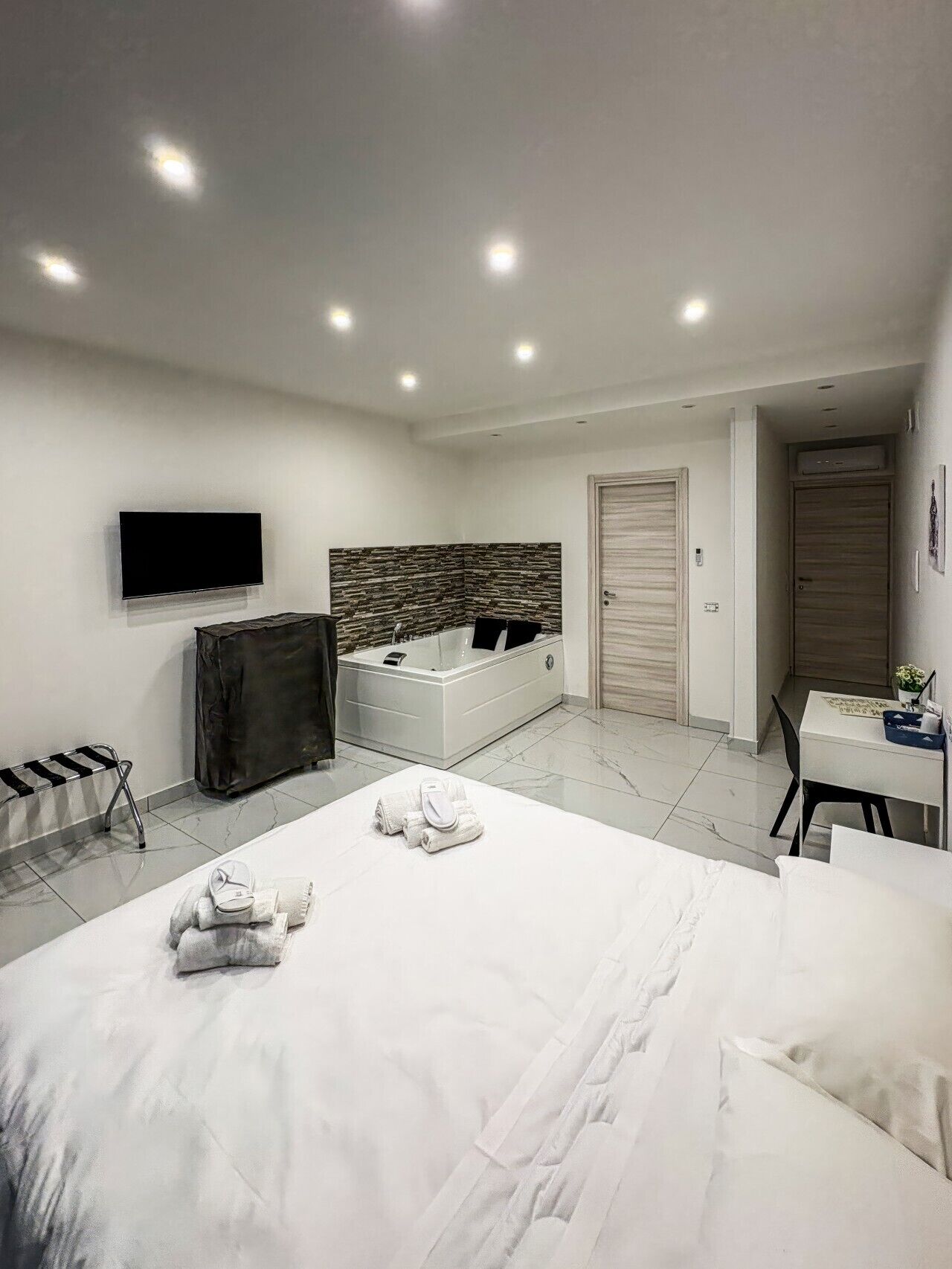 A modern bedroom with a large bed, a TV mounted on the wall, a small desk, and a shower area.. B&B Patty and Mary - Room with Jacuzzi