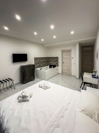 A modern bedroom with a large bed, a TV mounted on the wall, a small desk, and a shower area.. B&B Patty and Mary - Room with Jacuzzi