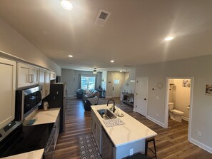 Eine moderne Küche mit einer zentralen Kochinsel, ein Essbereich mit einer Couch und Blick zum Wohnzimmer.