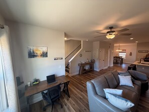 A spacious living area with a wooden floor, a gray leather couch, a dining table, and a staircase leading to another level. - Brand New Townhome, 3 Bed/2.5 Bath Close to Furman, NGU, SRT & Greenville! (Greenville)