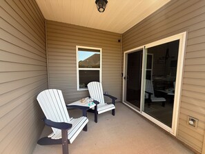 Eine überdachte Terrasse mit zwei Adirondack-Stühlen und einem kleinen Tisch, einer Schiebetür und einem Fenster.