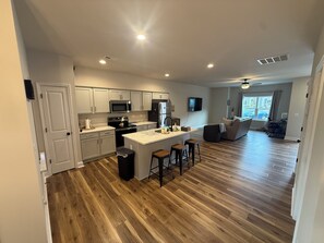 A modern kitchen with white cabinets, a central island with stools, and a dining area with a sofa and chairs. - Brand New Townhome, 3 Bed/2.5 Bath Close to Furman, NGU, SRT & Greenville! (Greenville)