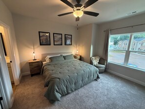 A bedroom with a bed, bedside lamps, a ceiling fan, and a window with a view of buildings. - Brand New Townhome, 3 Bed/2.5 Bath Close to Furman, NGU, SRT & Greenville! (Greenville)
