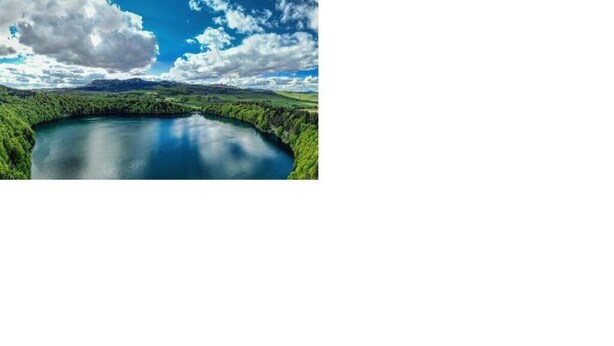 A natural landscape with a lake surrounded by dense greenery and mountains in the background. - Studio PavinChic, cozy & ideally located (Clermont-Ferrand)