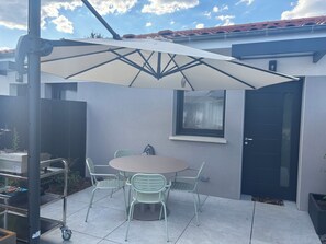 Eine Terrasse mit Tisch, Stühlen, einem großen Sonnenschirm, einer Tür und einem Fenster.