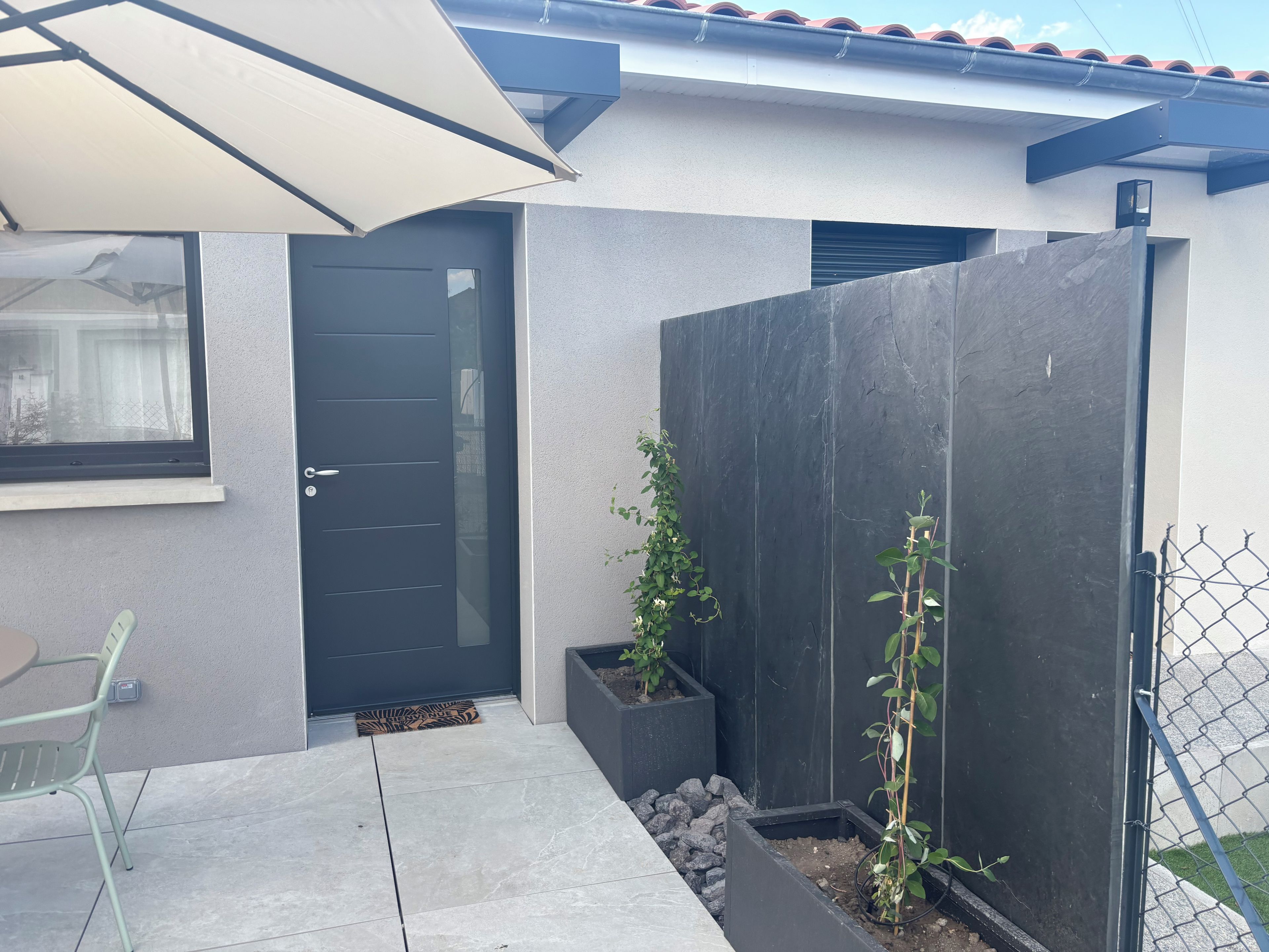 A modern outdoor area with a door, a potted plant, a chair, and a concrete floor.