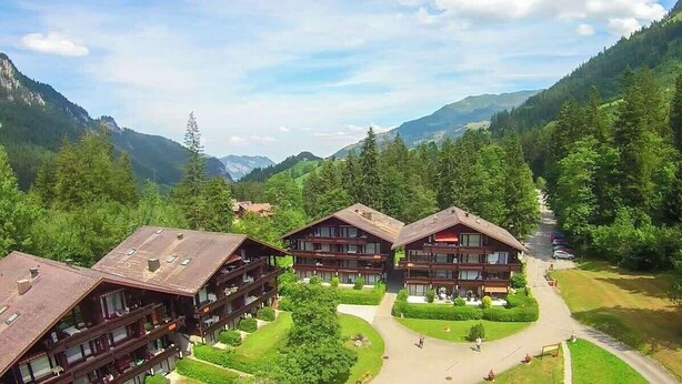 A mountain lodge with multiple wooden buildings, a central courtyard, and a view of surrounding forest and mountains. - Cozy Alpine Studio in Wiriehorn with Parking (Diemtigen)