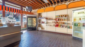 A restaurant interior with a brick floor, a counter with a basket, a refrigerator stocked with beverages, and shelves with snacks. - Cozy Alpine Studio in Wiriehorn with Parking (Diemtigen)