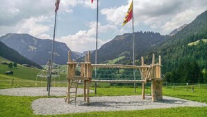 A playground with a swing set and climbing structure in a grassy area with mountains in the background. - Cozy Alpine Studio in Wiriehorn with Parking (Diemtigen)