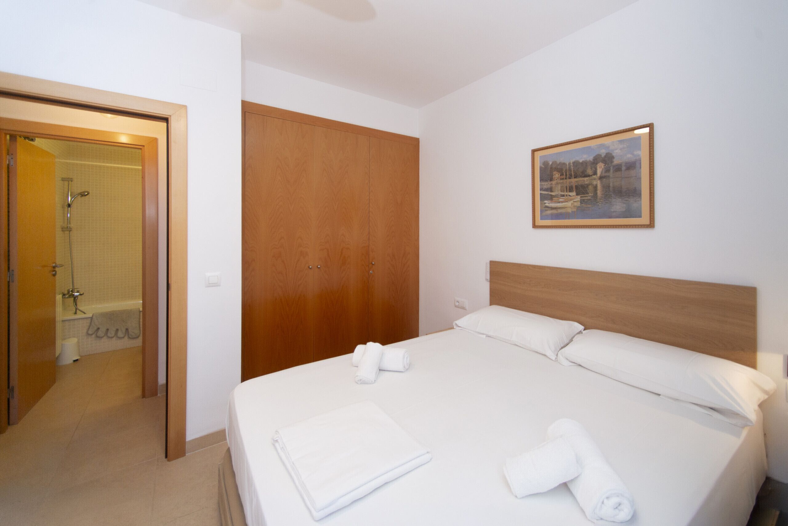 Una habitación de hotel con cama, un armario de madera, un cuadro en la pared y zona de ducha.