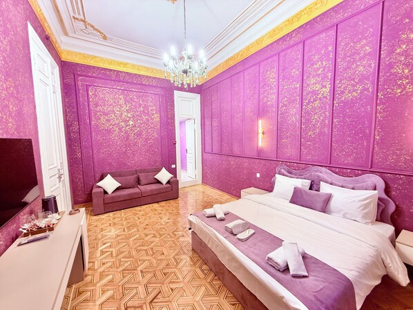Quarto com uma cama grande, um sofá, uma TV e um candelabro.