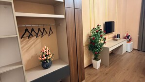 Quarto moderno com guarda-roupa de madeira, prateleira com peças penduradas, secretária com televisão de tela plana e um vaso de plantas.