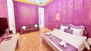 Quarto com uma cama grande, um sofá, uma TV e um candelabro.