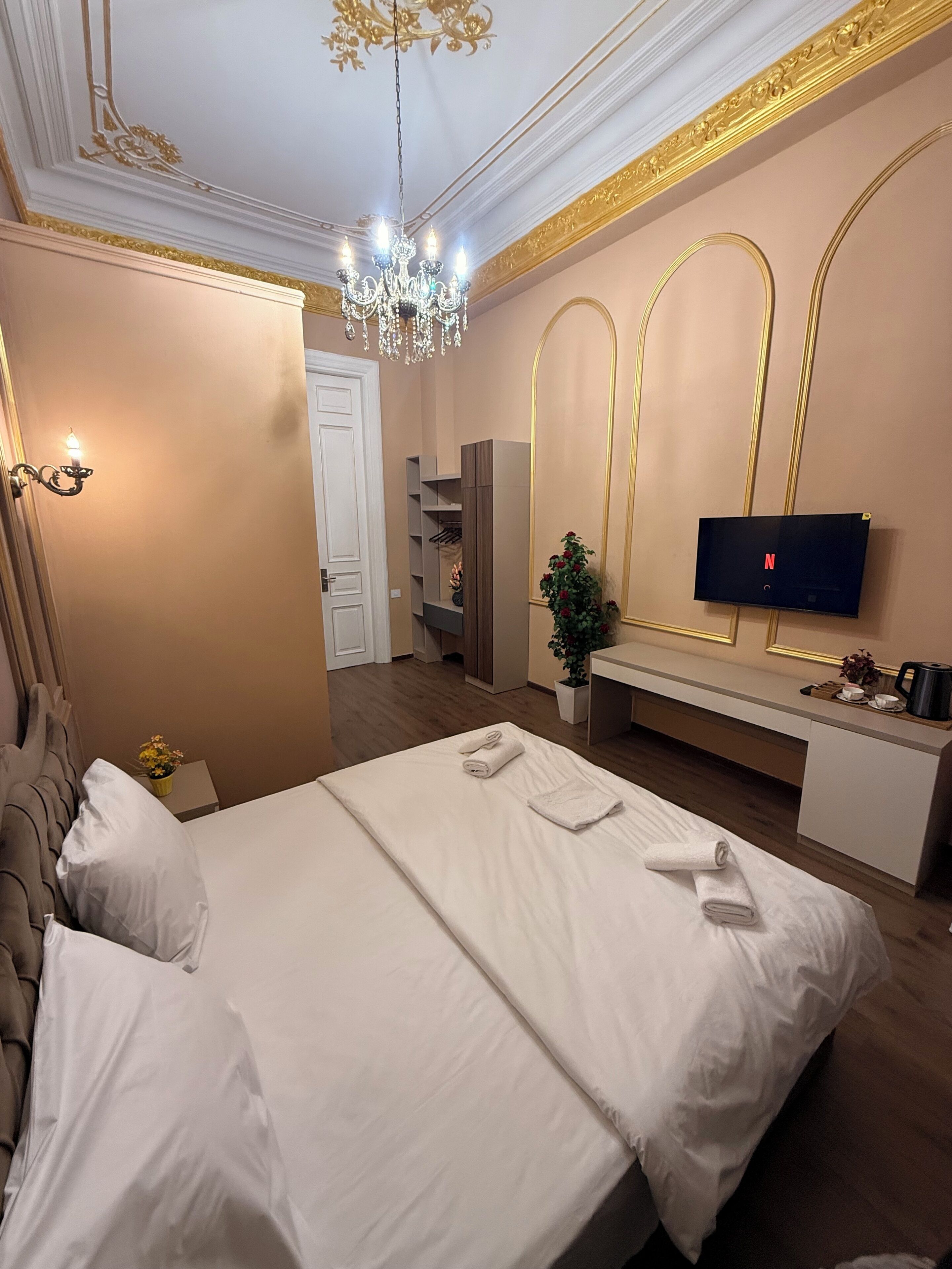 Ett hotellrum med en stor säng, en tv som är monterad på väggen, en kristallkrona och en växt.