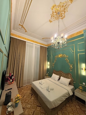 A hotel room with a large bed, a chandelier, a nightstand, and a window with curtains. - Crown Palace Hotel Baku (Baku)
