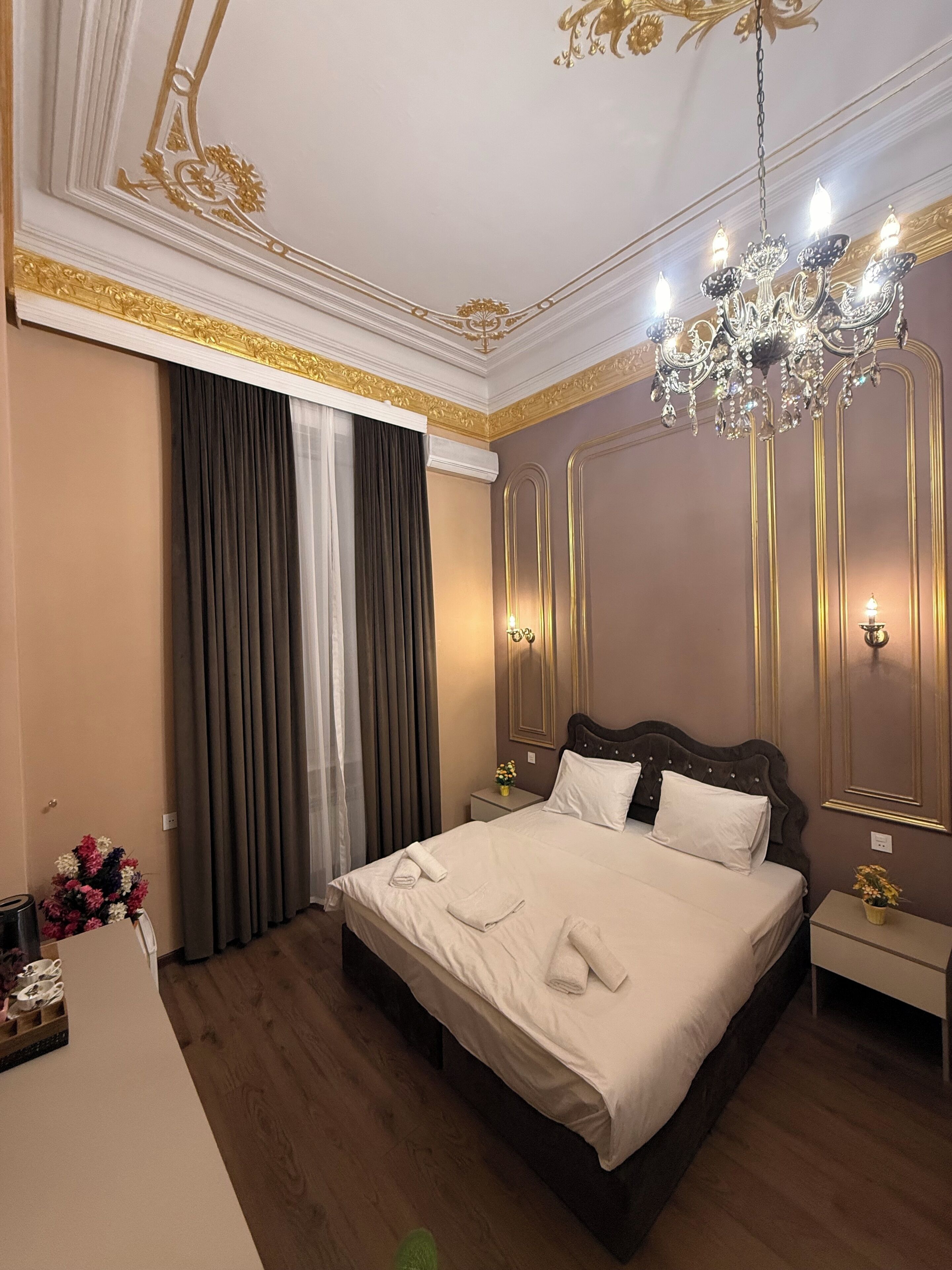 A hotel room with a large bed, a chandelier, a nightstand, and a mirror.