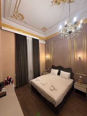 A hotel room with a large bed, a chandelier, a nightstand, and a mirror. - Crown Palace Hotel Baku (Baku)
