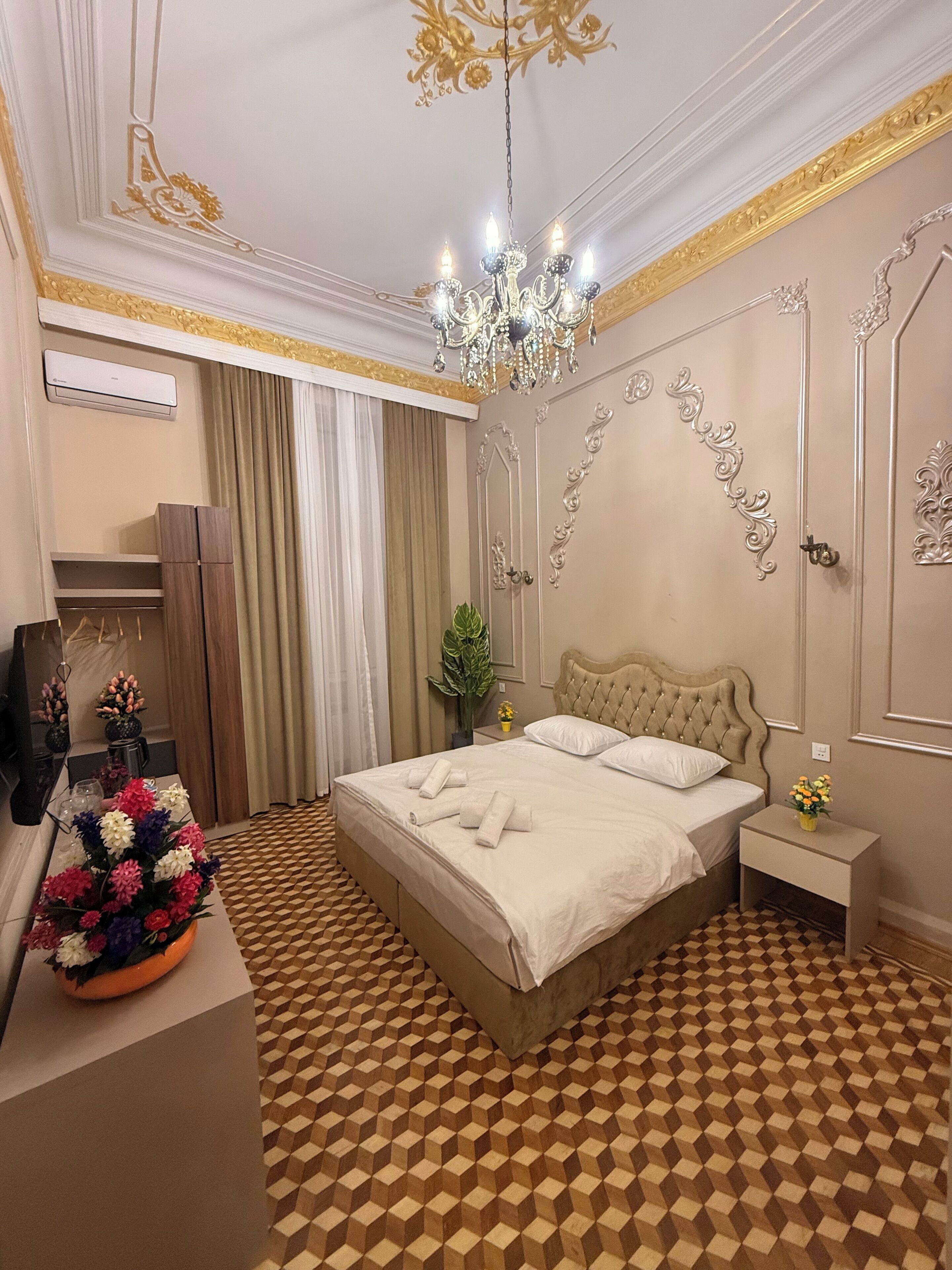 A hotel room with a checkered floor, a bed with white linens, a chandelier, and a mirror.