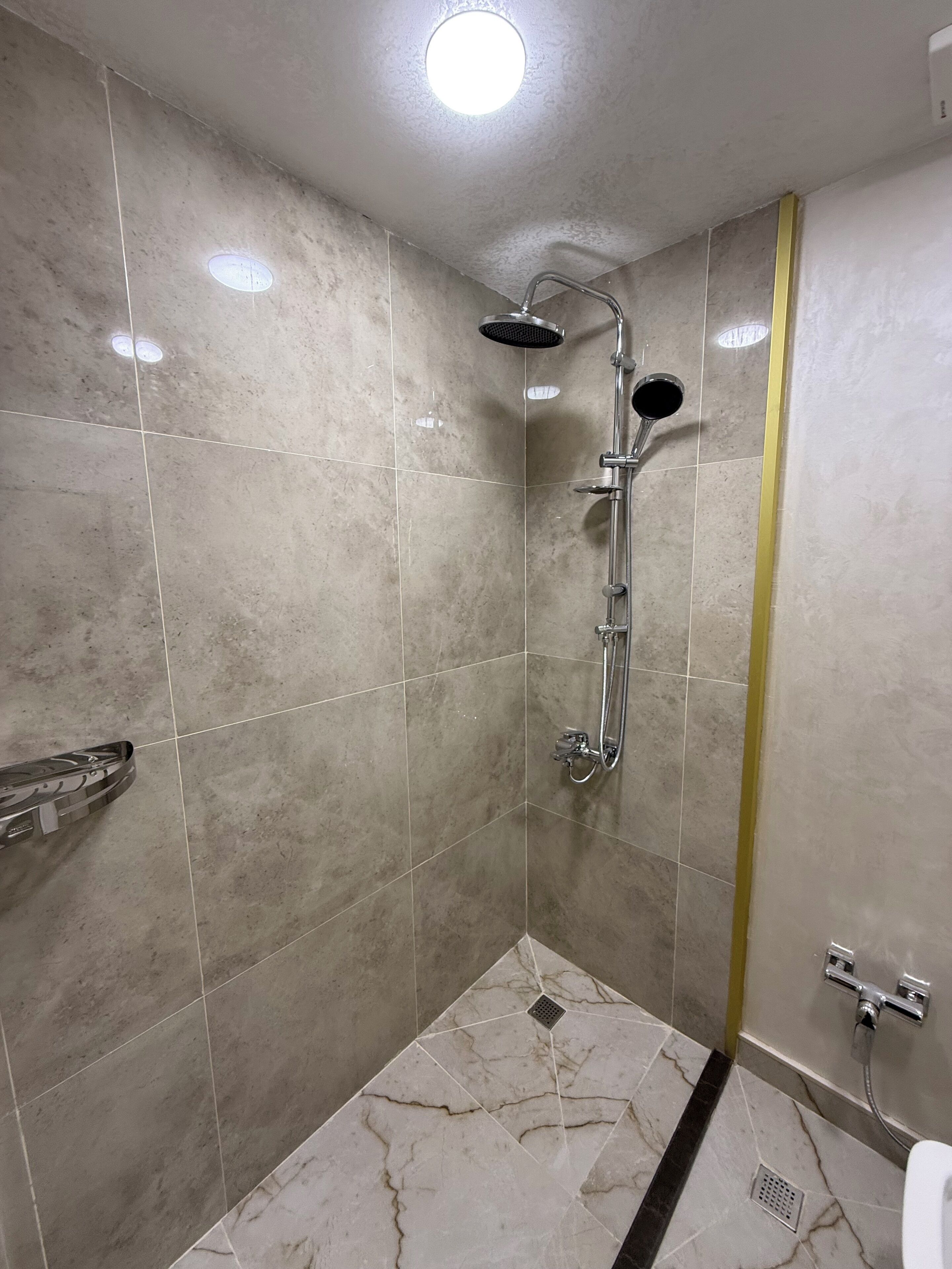 Une salle de bain avec une douche, des murs carrelés et un drain.