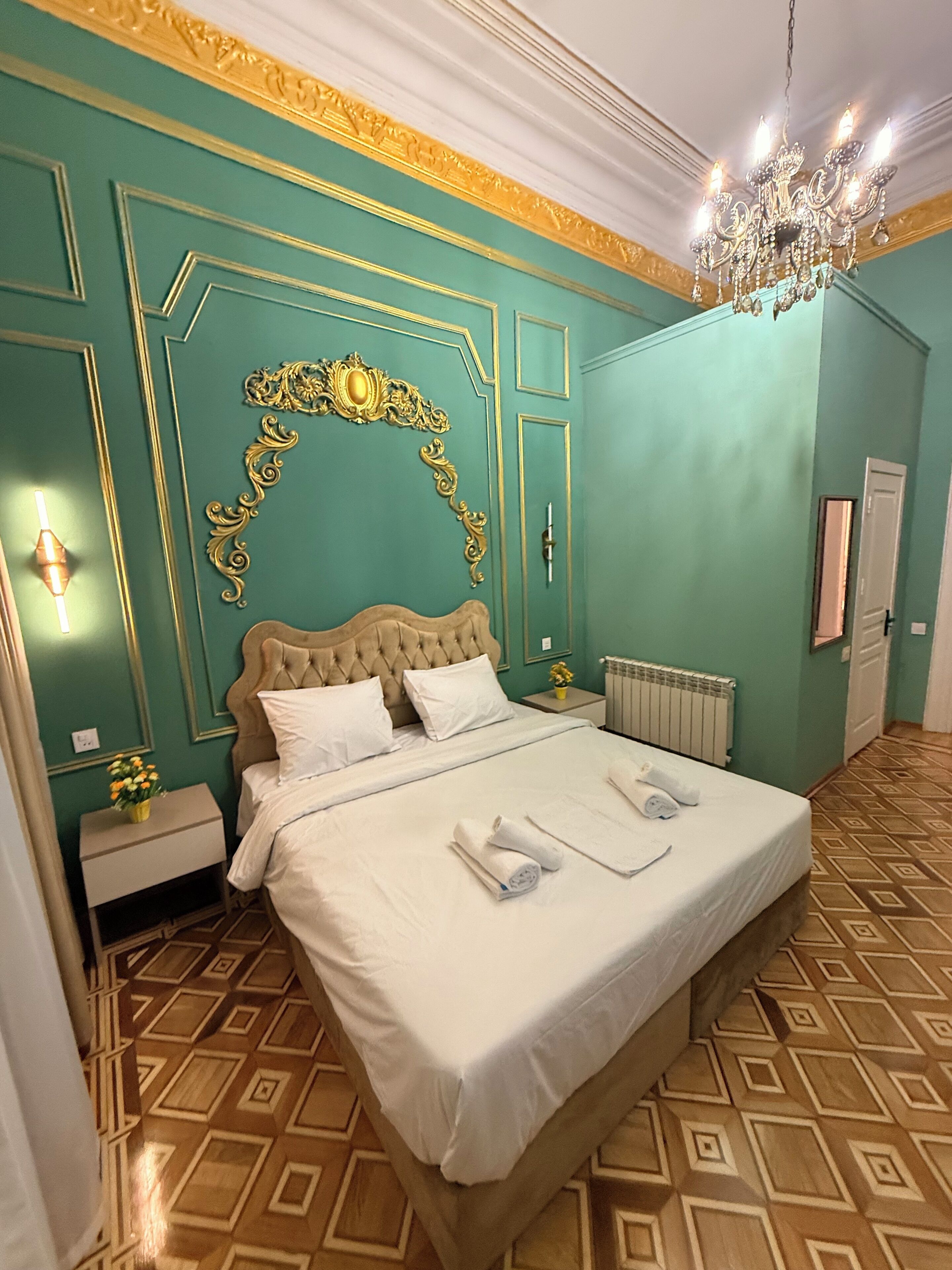 Une chambre d’hôtel avec un grand lit, un lustre, une arche décorative au mur et un sol à motifs.