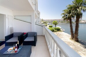 A balcony with outdoor seating, a table with a bottle and glasses, and a view of the sea and buildings. - WELCS APARTMENT 380 EMP with terrace and parking (Empuriabrava)