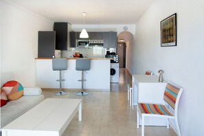 A modern kitchen with a microwave, oven, and sink. There is a dining area with a white table and chairs. A sofa and a colorful cushion are also visible. - WELCS APARTMENT 380 EMP with terrace and parking (Empuriabrava)