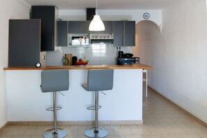 Een moderne keuken met grijze kastjes, een wit aanrecht en twee barkrukken.