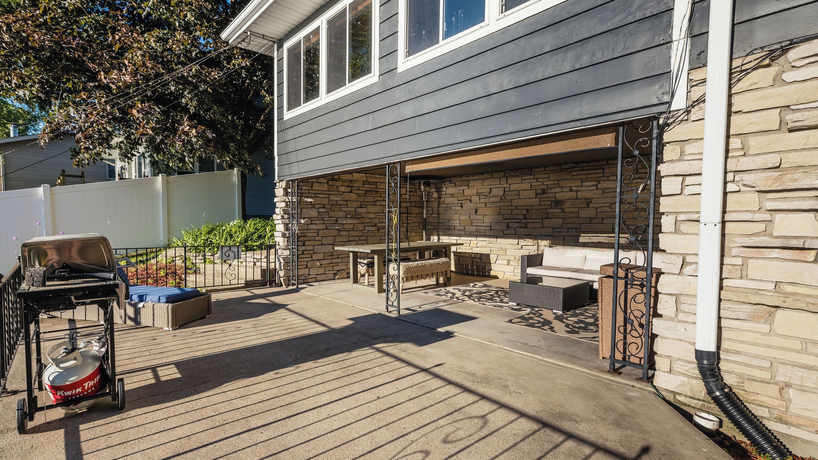 An outdoor patio with a grill, seating, and a stone wall backdrop.