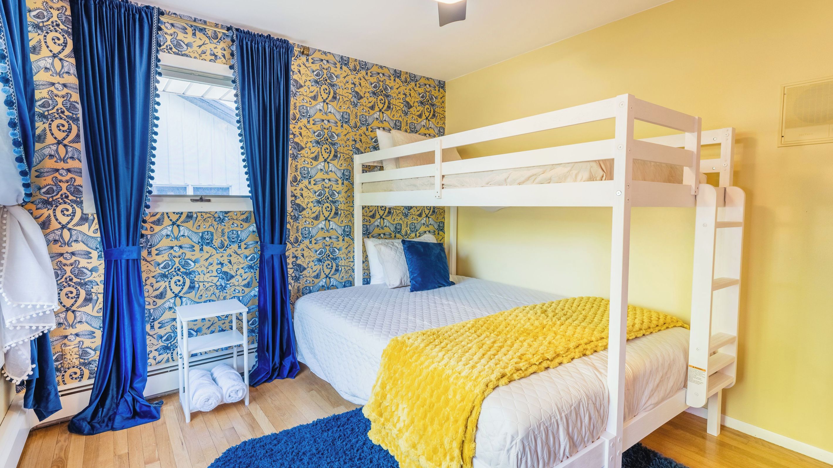 A bunk bed room with a patterned wallpaper, a small white shelf, and a blue curtain.
