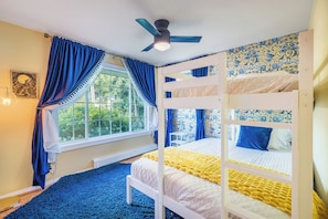 Ein Zimmer mit Etagenbetten, einem fensterbelaubten Fenster, einem Deckenventilator und einer Wand mit einem gemusterten Dekor.