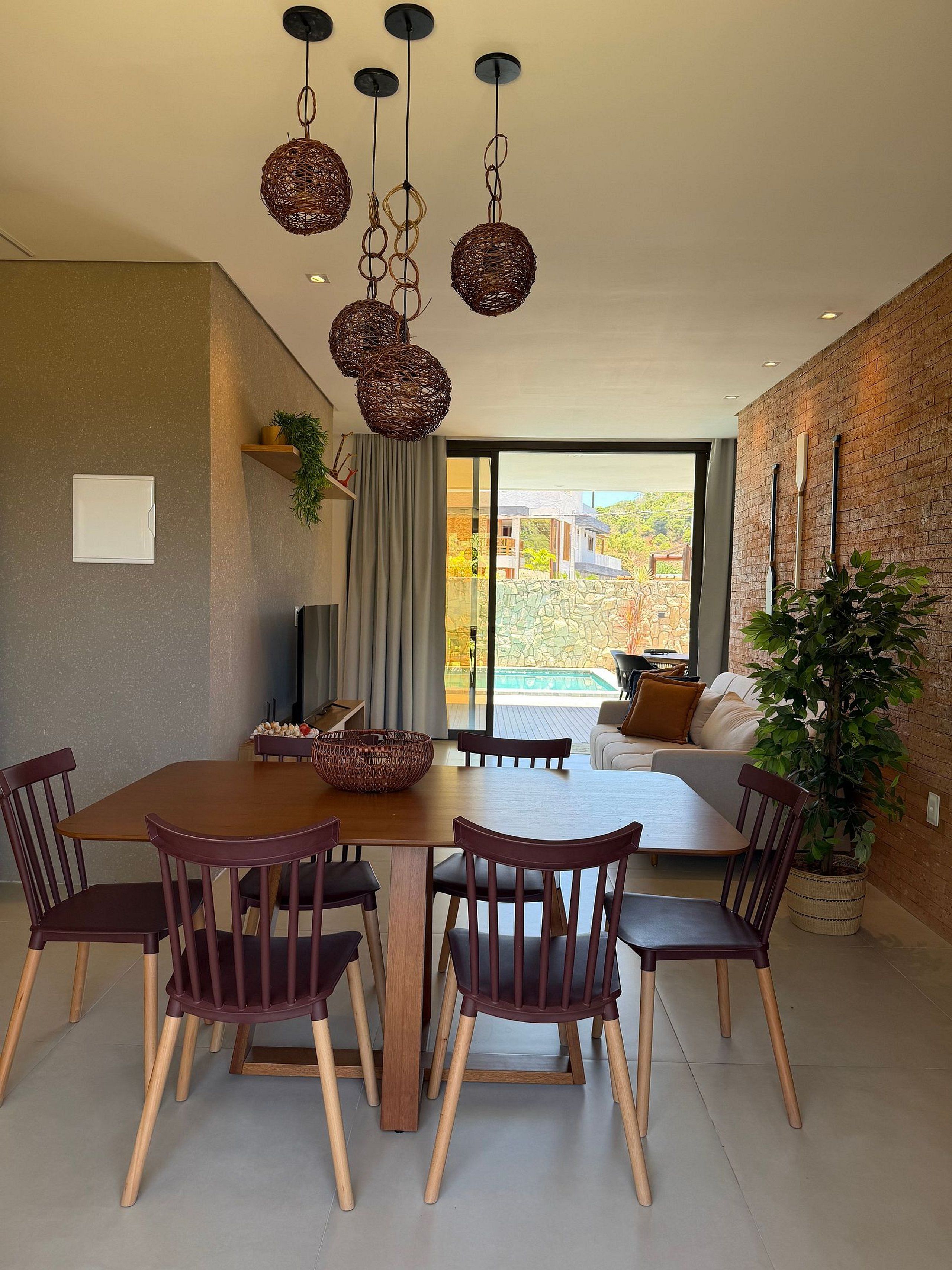 Un coin repas avec une table et des chaises en bois, un luminaire suspendu et une vue sur une piscine, visible à travers une porte vitrée.