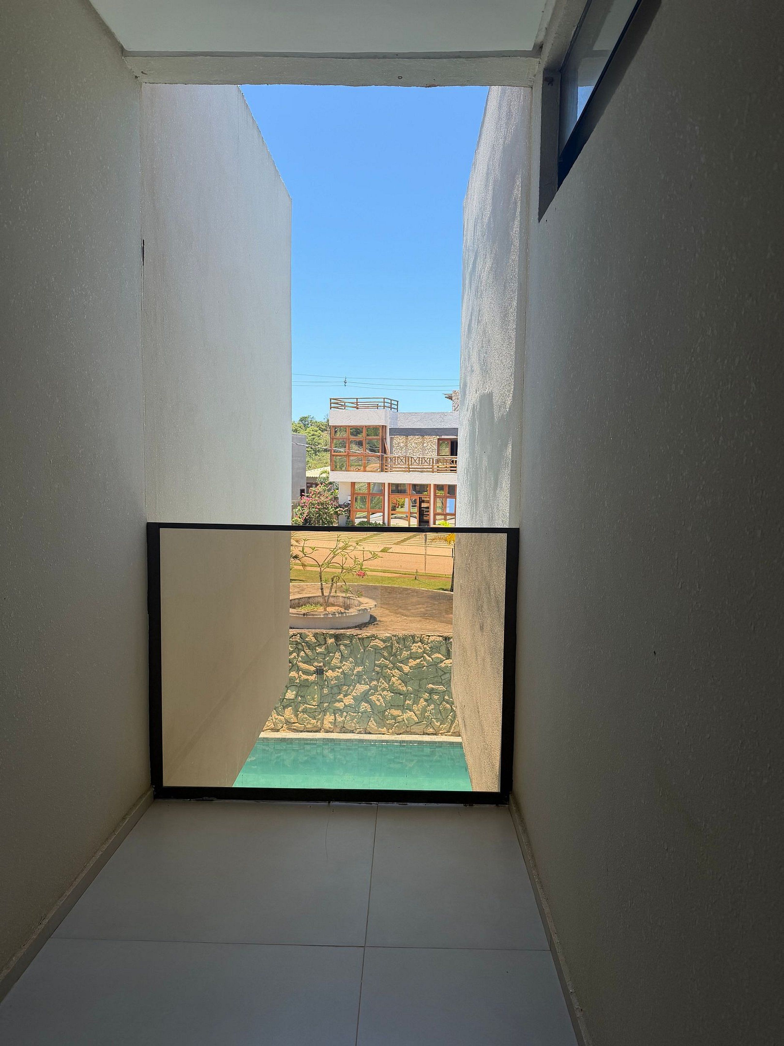 A narrow corridor with a view of a building and a small outdoor area with a stone wall and a plant.