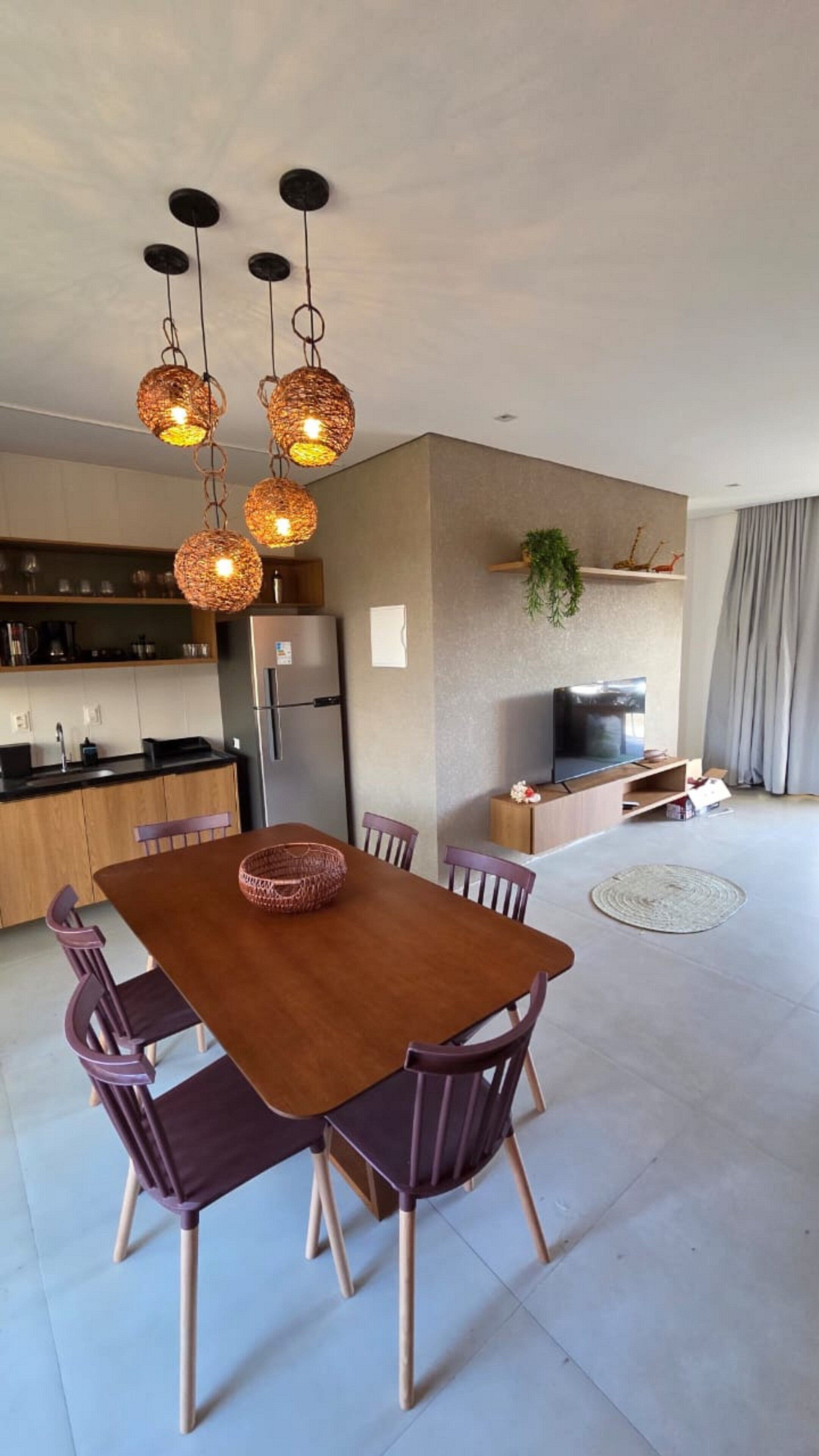 A modern kitchen with a dining area, a refrigerator, a TV, and a plant.