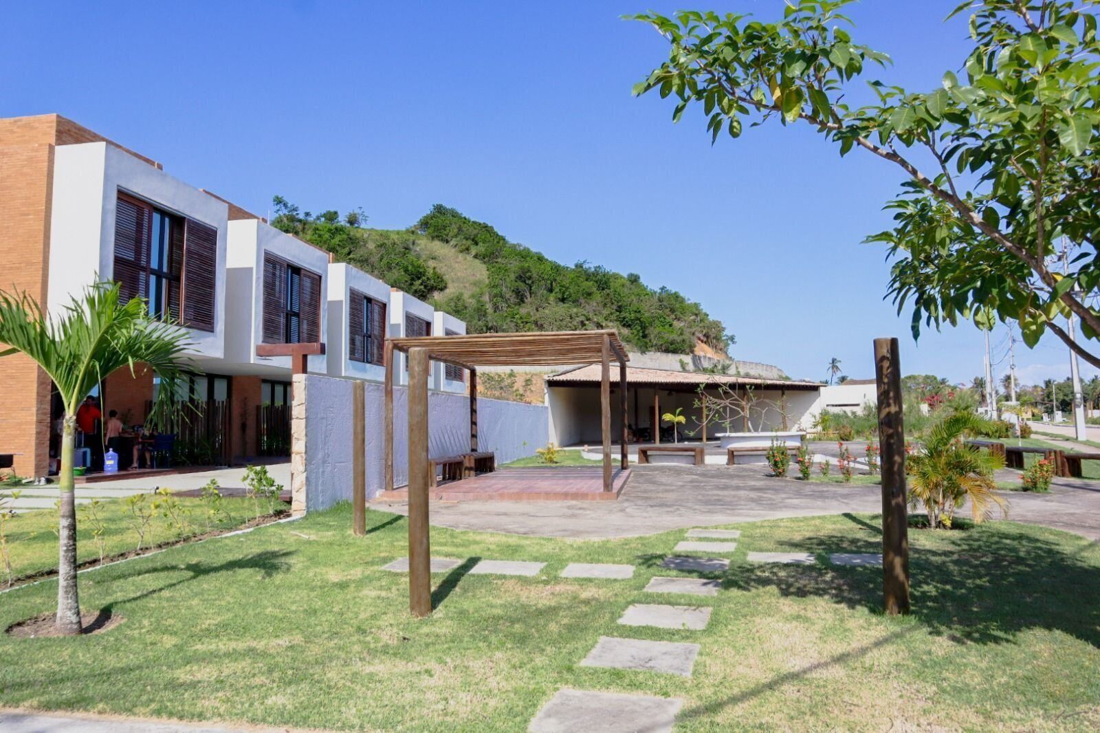 A modern building with a covered outdoor seating area, a grassy courtyard, and a hillside in the background.
