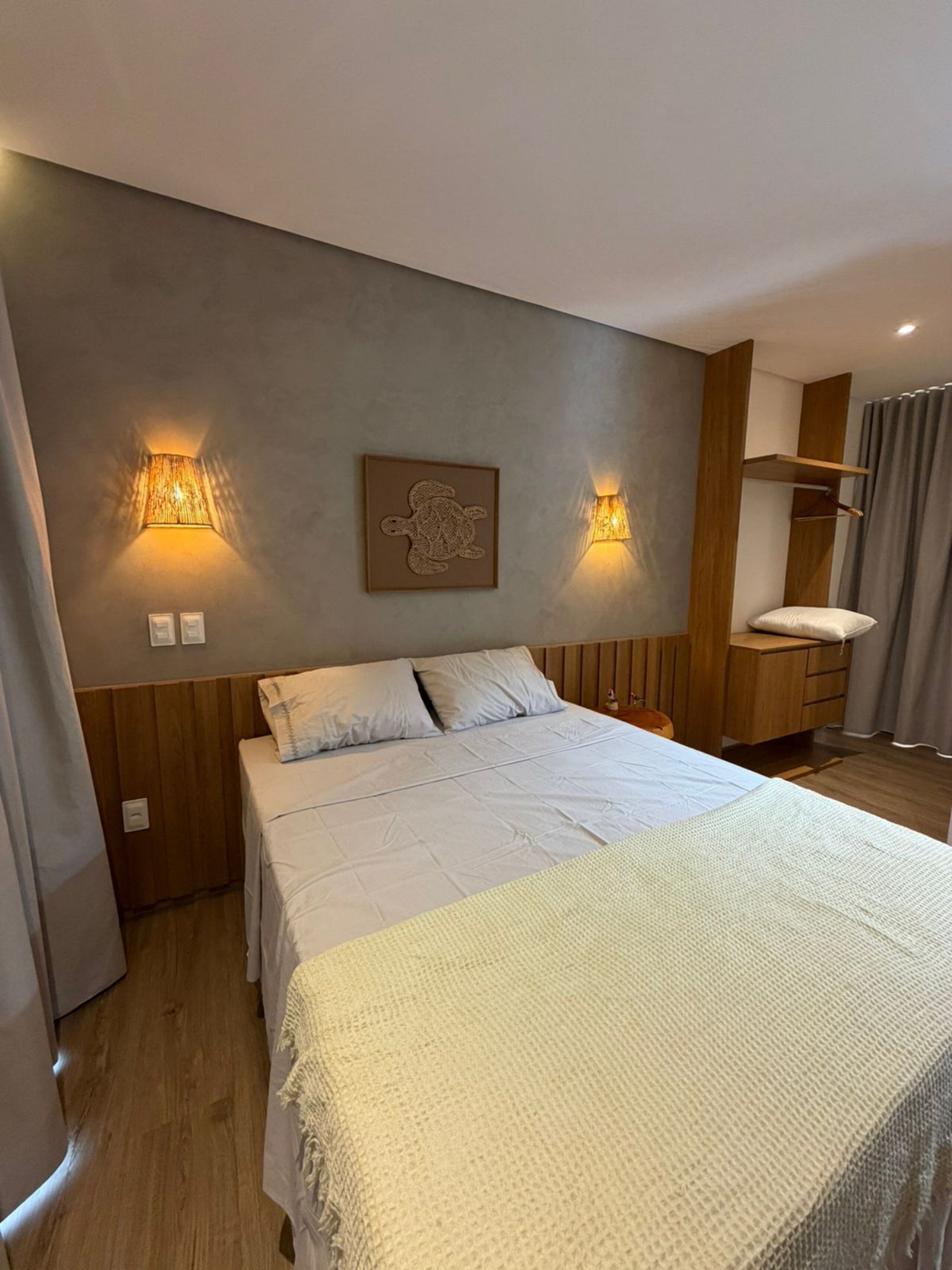 Ein Schlafzimmer mit einem Bett, zwei Wandlampen, einem Holzkopfende, einem Nachttisch und einem an der Wand befestigten Regal.