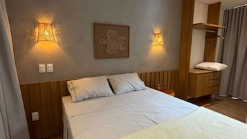 Ein Schlafzimmer mit einem Bett, zwei Wandlampen, einem Holzkopfende, einem Nachttisch und einem an der Wand befestigten Regal.