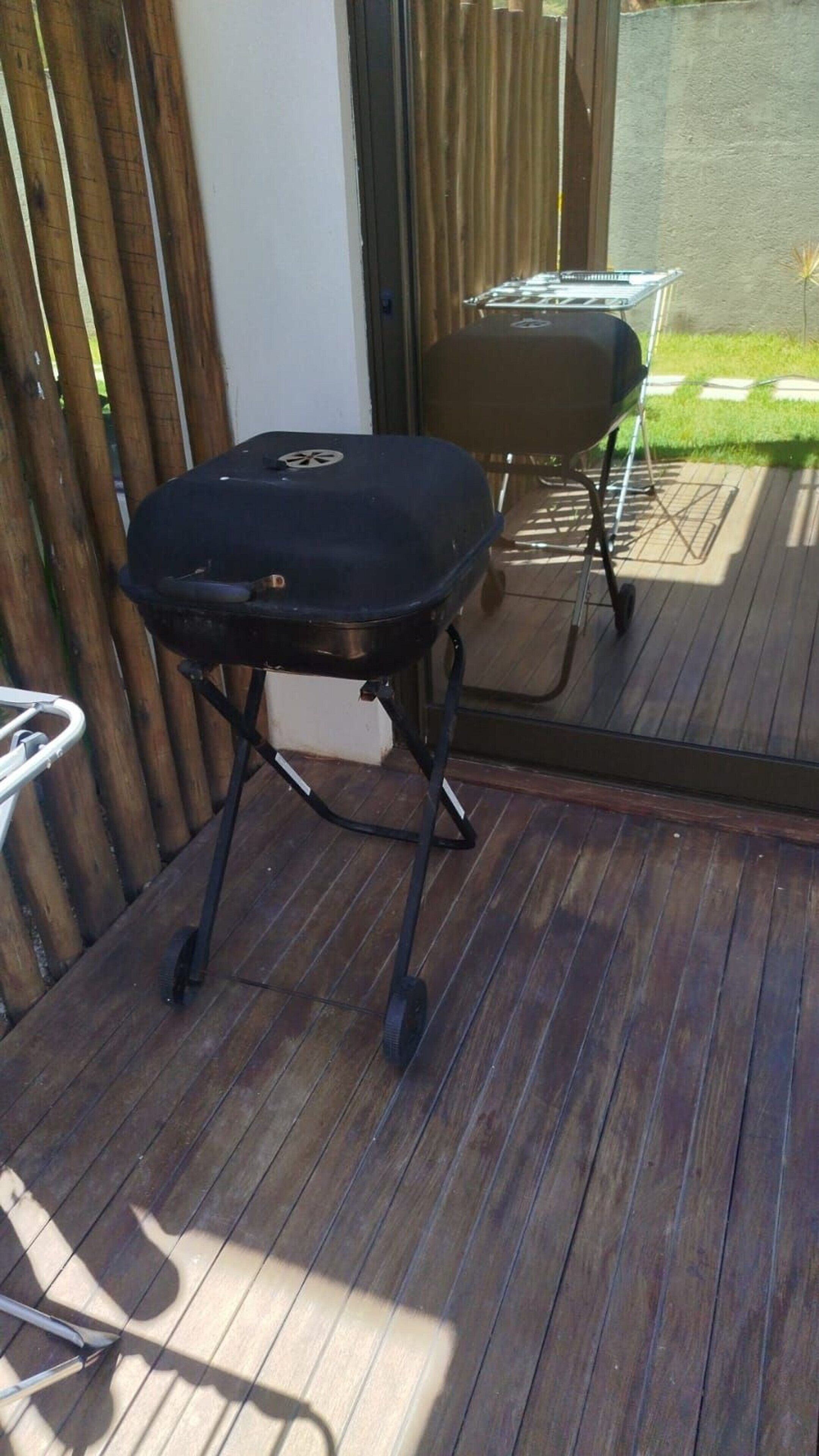 Un barbecue sur une terrasse en bois, avec une porte vitrée donnant sur un espace patio.