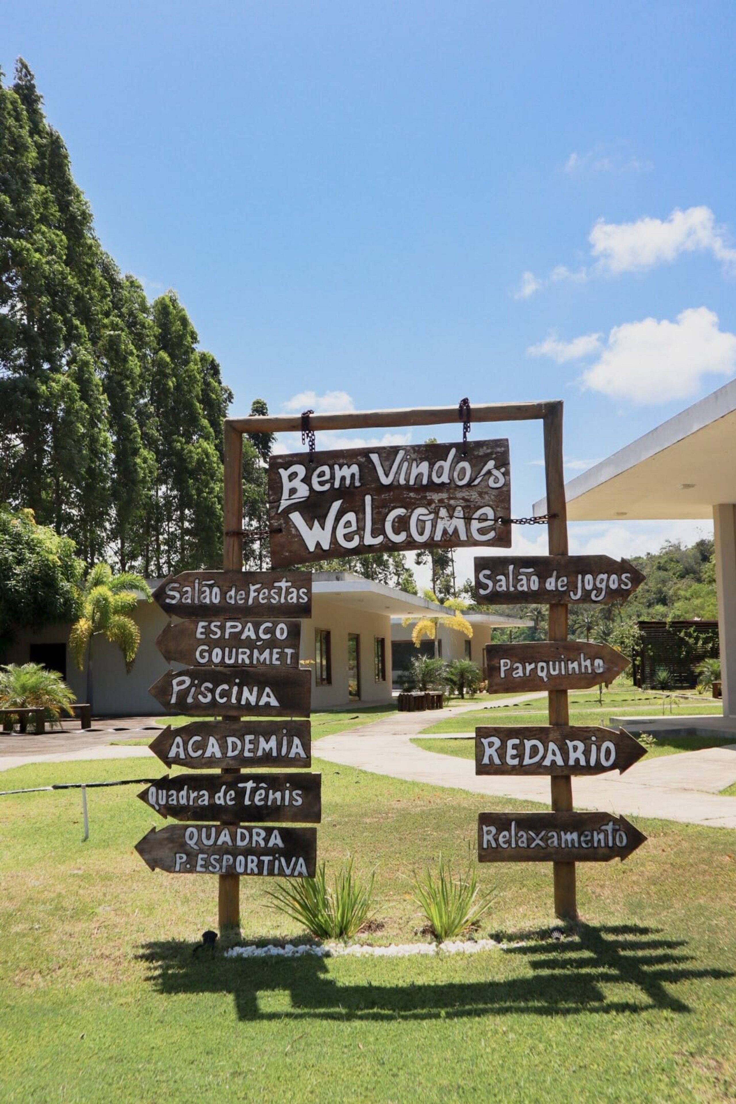 A wooden signpost with multiple directional arrows pointing to various amenities such as a swimming pool, tennis courts, and a relaxation area.