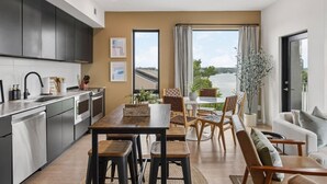 Una cocina moderna con armarios oscuros, un comedor con mesa y sillas de madera, y vista a una masa de agua a través de amplios ventanales.