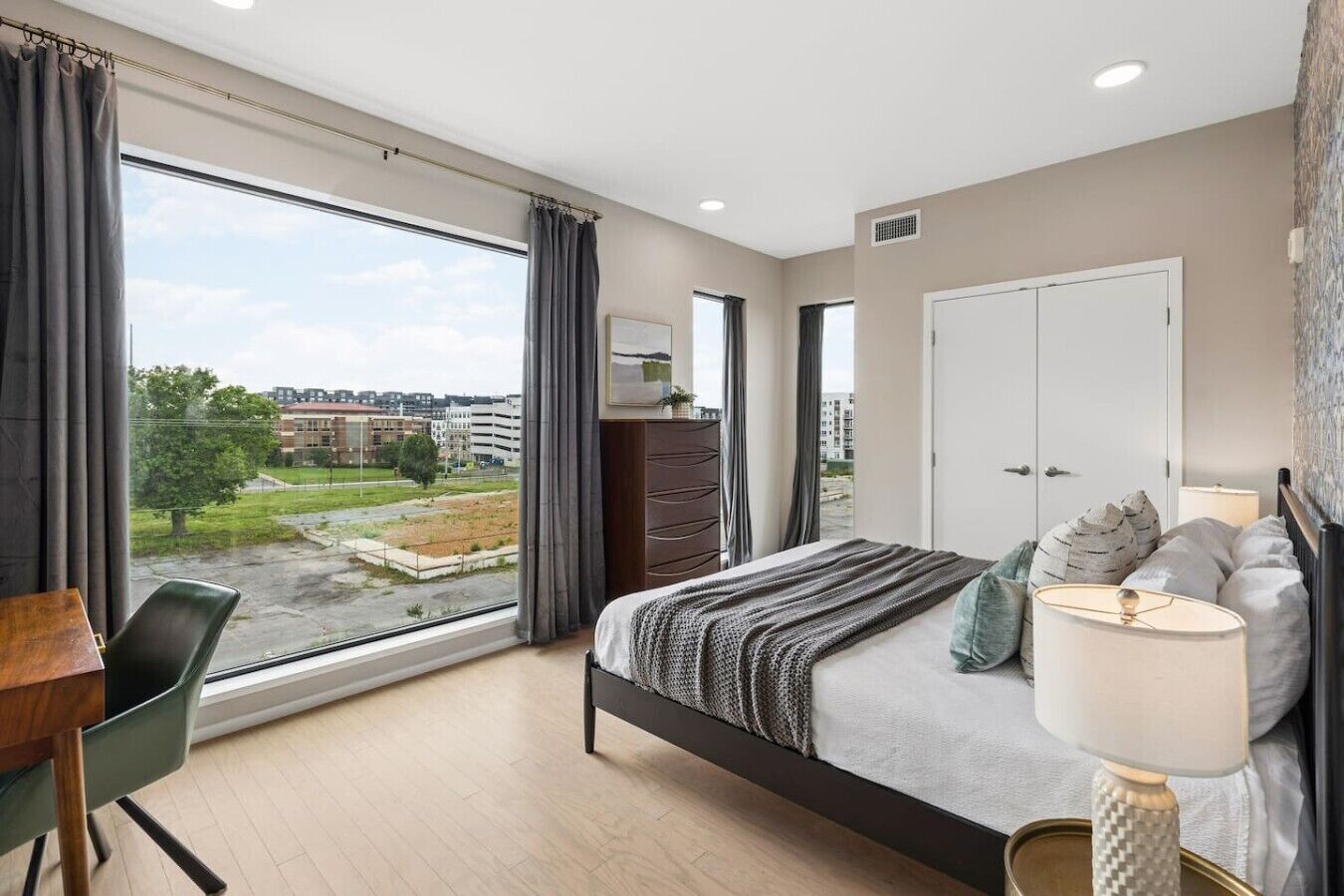 A modern bedroom with a large window, a bed, a dresser, and a desk with a chair.