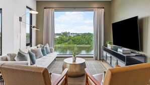 Una sala de estar moderna con sofá, sillones, televisor y vista a un lago.