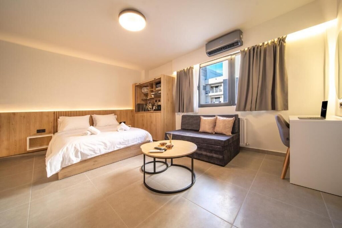 A modern hotel room with a bed, sofa, round table, and built-in storage.