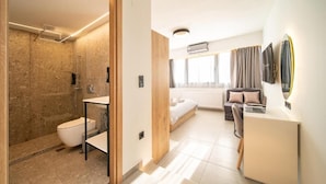 Een moderne hotelkamer met douche, toilet, wastafel, bed, bureau en een grote spiegel.