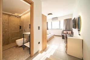 Ein modernes Hotelzimmer mit Dusche, WC, Waschbecken, Bett, Schreibtisch und einem großen Spiegel.