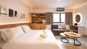 Een hotelkamer met een bed, een sofa, een bureau met een computer, een magnetron en een kitchenette.