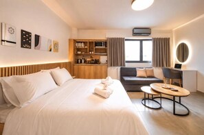Ein Hotelzimmer mit einem Bett, einem Sofa, einem Schreibtisch mit Computer, einer Mikrowelle und einer kleinen Küchenzeile.