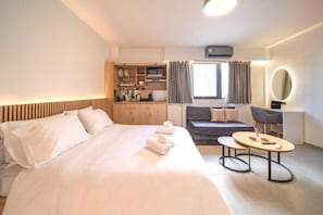 Ein Hotelzimmer mit Bett, Sofa, kleinem Tisch, einer Küchenzeile und einem Fenster mit Vorhängen.