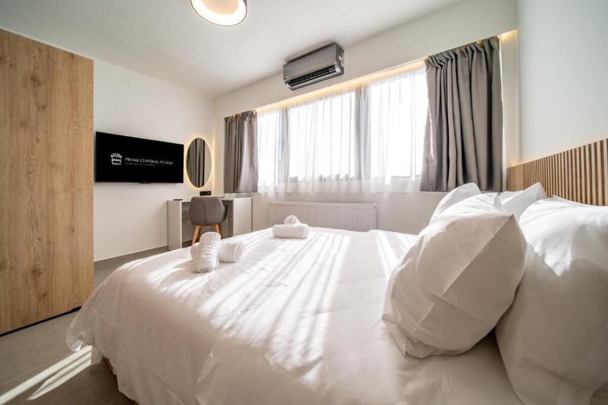 A hotel room with a bed, a TV, a window with curtains, and an air conditioning unit.